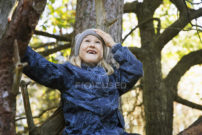 Chica sonriente sentada en el árbol - foto de stock