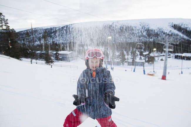 Girl in helmet and jacket throwing snow on mountain — Stock Photo