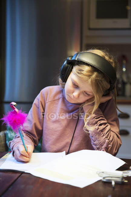 Дівчина з навушниками навчається за кухонним столом — стокове фото