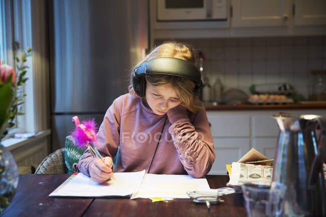 Дівчина з навушниками навчається за кухонним столом — стокове фото