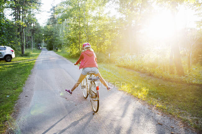 Girl riding bicycle on rural road during sunset — Foto stock