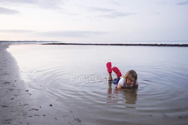 Girl lying in shallow water at beach — Fotografia de Stock