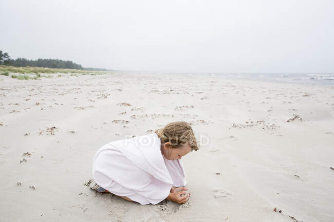 Fille enveloppée dans une serviette jouant sur la plage — Photo de stock