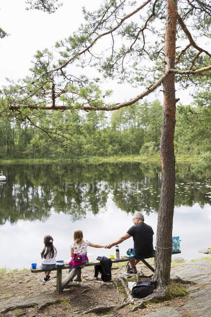 Family sitting on bench by lake — Fotografia de Stock