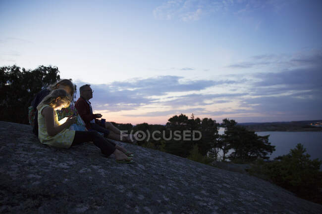 Family sitting on rock by coast during sunset — Stock Photo
