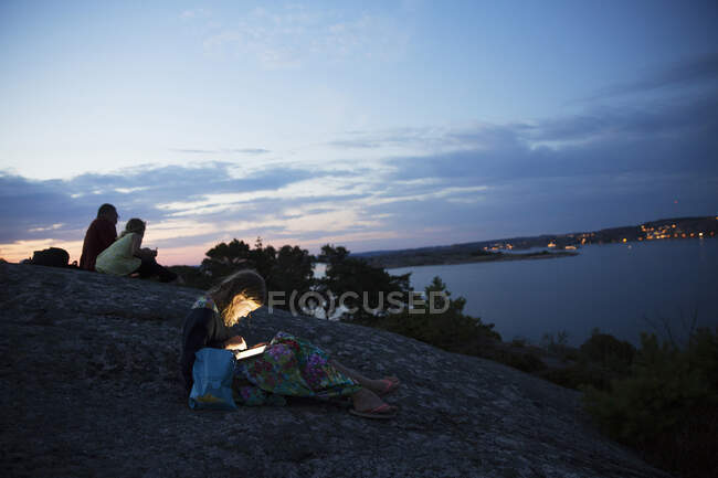 Family sitting on rock by coast during sunset — Stockfoto