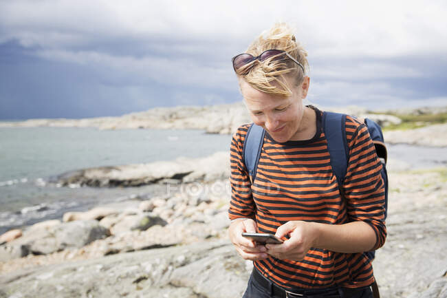 Woman with smart phone hiking by sea — Fotografia de Stock