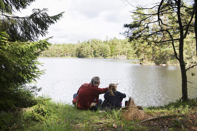 Отец и дочь сидят у озера — стоковое фото