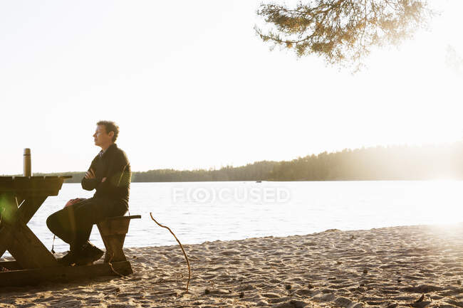 Woman sitting at picnic table by lake during sunset — Fotografia de Stock