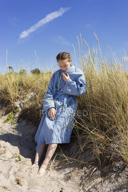 Teenage girl in bathrobe by grass on beach dune - foto de stock