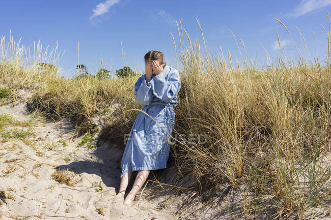 Teenage girl in bathrobe by grass on beach dune — Stockfoto