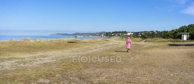 Donna in accappatoio rosa passeggiando in spiaggia — Foto stock