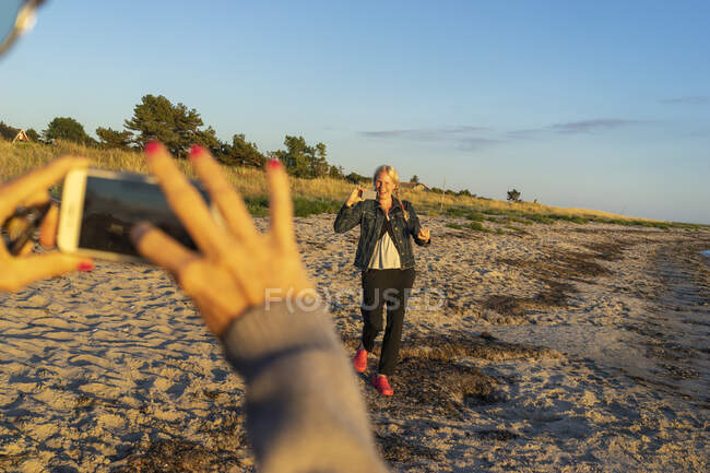 Hands of woman photographing friend with smartphone on beach — Stock Photo