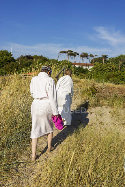 Girls in robes walking on dunes at beach — Stock Photo