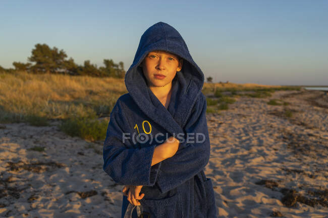 Garçon en peignoir à capuche sur la plage au coucher du soleil — Photo de stock