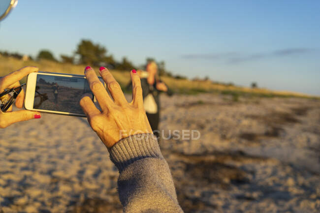 Mains de femme photographier ami avec smartphone sur la plage — Photo de stock