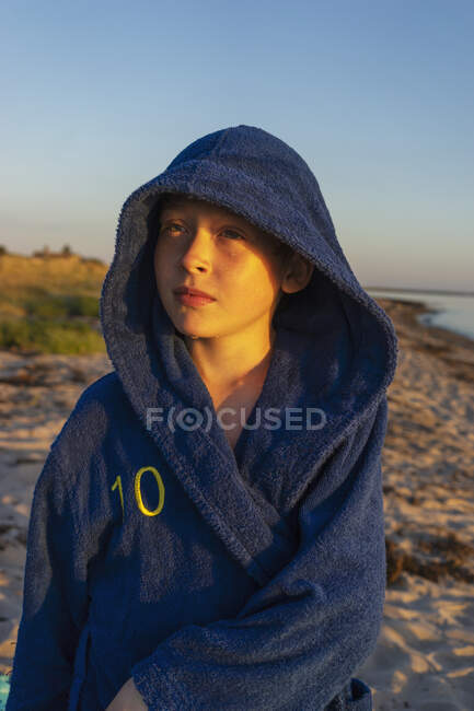 Boy in hooded bathrobe on beach at sunset — Foto stock