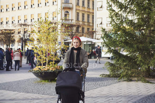 Woman holding stroller on city street — Fotografia de Stock