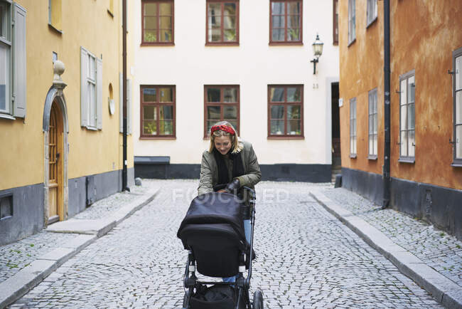 Woman walking with stroller on city street — Stock Photo