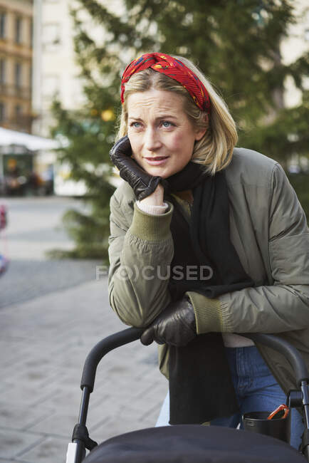 Woman leaning on stroller in city — Stock Photo