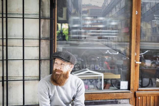 Bearded man wearing flat cap outside store — Stock Photo