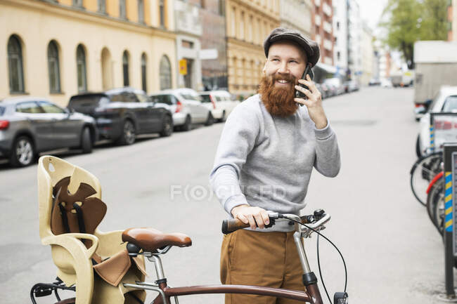 Чоловік по телефону штовхає велосипед на міську вулицю — стокове фото