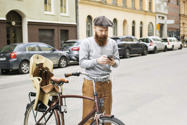 Man using smart phone by bicycle on city street — Stockfoto