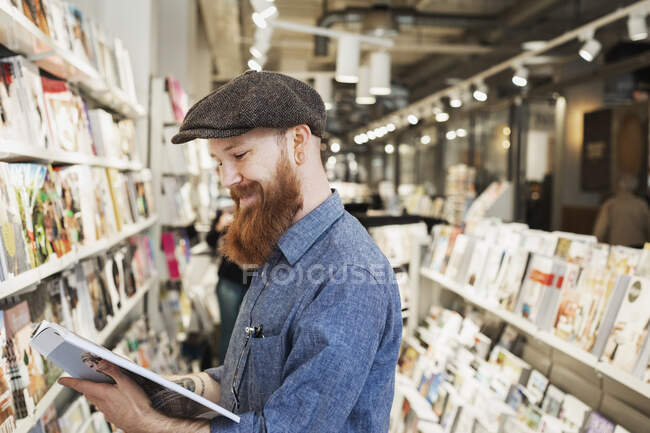 Bearded man reading magazine in store - foto de stock