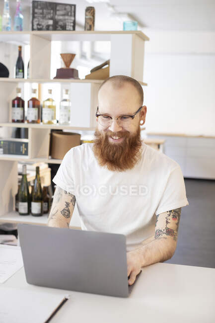 Smiling man with beard using laptop at table - foto de stock