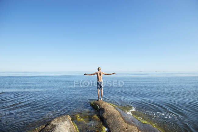 Young man standing on rock by sea — Stockfoto