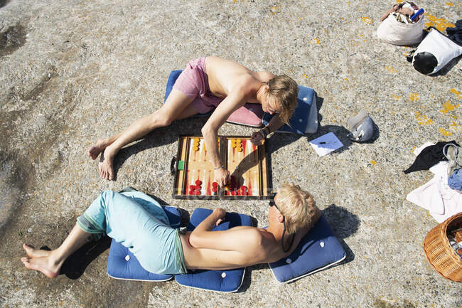 Young men lying down playing backgammon on rock - foto de stock