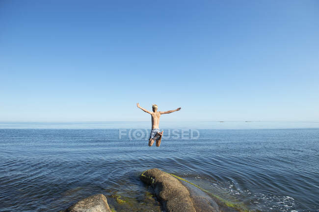 Young man jumping off rock by sea — Stock Photo