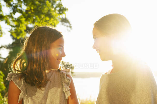 Meninas sorrindo pela árvore na luz do sol — Fotografia de Stock