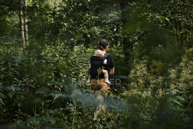 Woman walking through forest with daughter in baby carrier — Photo de stock