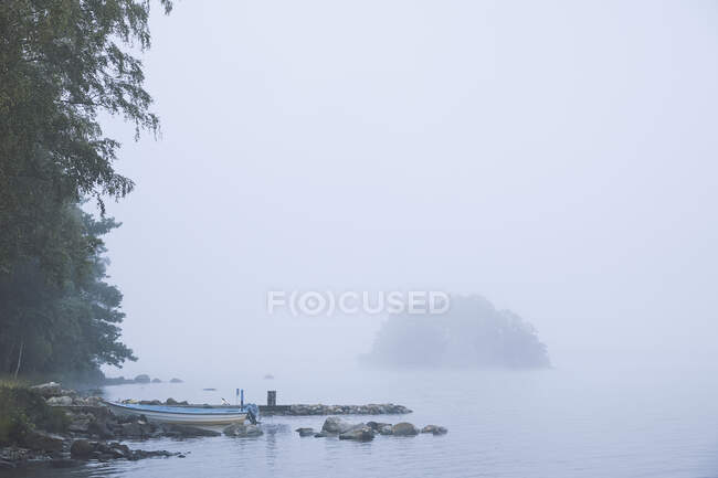 Boat on shore of foggy lake — Stockfoto