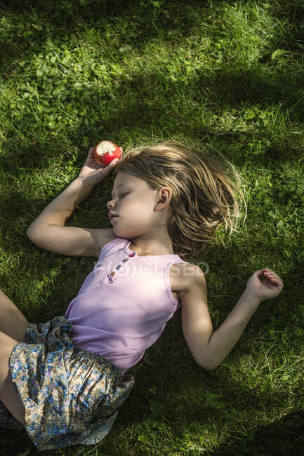 Girl with apple sleeping in grass - foto de stock