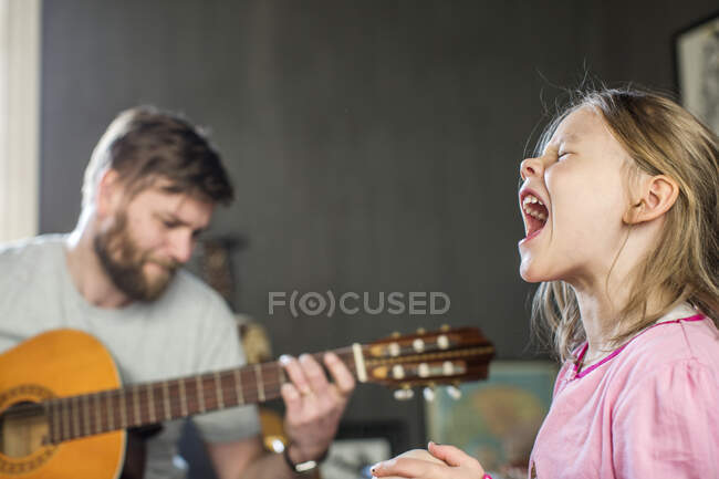 Девушка поет, пока ее отец играет на гитаре — стоковое фото