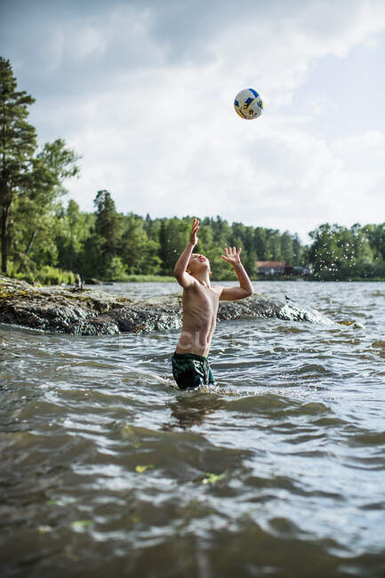 Мальчик играет с мячом в озере — стоковое фото