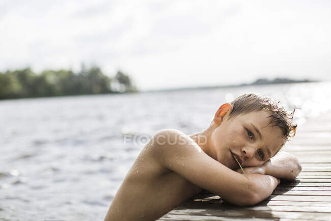 Niño apoyado en embarcadero en el lago - foto de stock