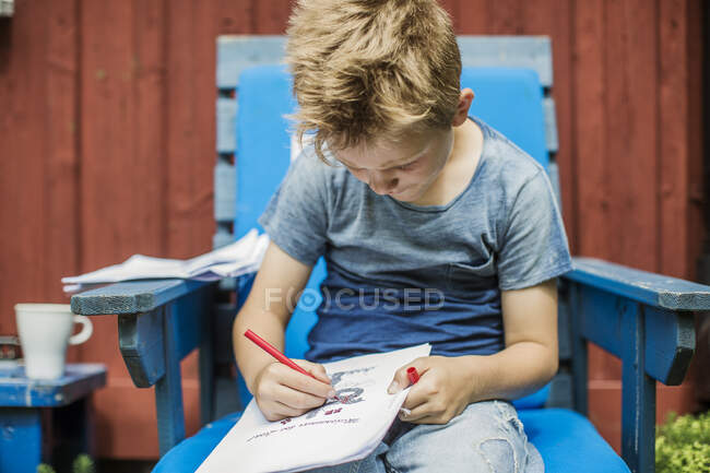 Menino desenho em cadeira azul ao ar livre — Fotografia de Stock