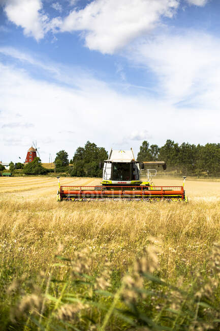 Combine harvester on farm with windmill — Stock Photo