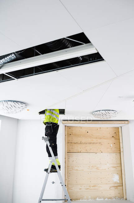Construction worker on ladder working in ceiling — Fotografia de Stock