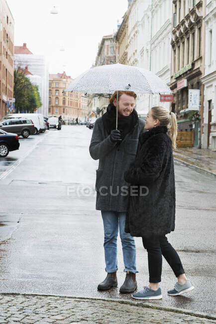 Young couple with umbrella on city street — Fotografia de Stock