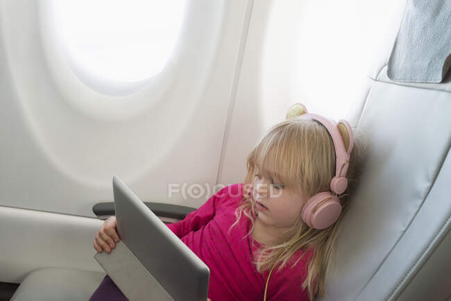 Дівчинка з планшетом і навушниками сидить на літаку. — стокове фото