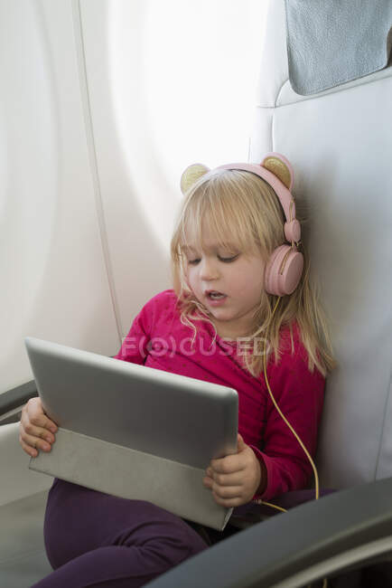 Girl with tablet and headphones sitting on airplane — Stockfoto