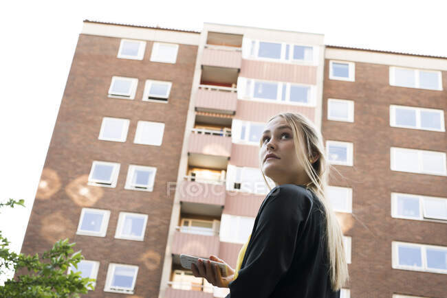 Young woman with smart phone by apartment building — Photo de stock