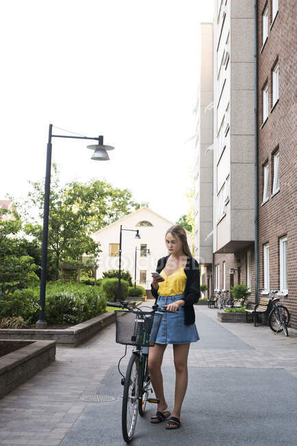 Молода жінка з розумним телефоном і велосипедом у місті. — стокове фото