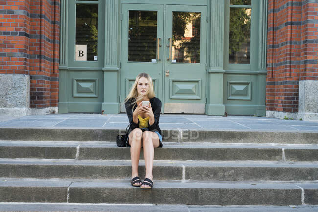 Young woman with smart phone sitting on steps — Stock Photo