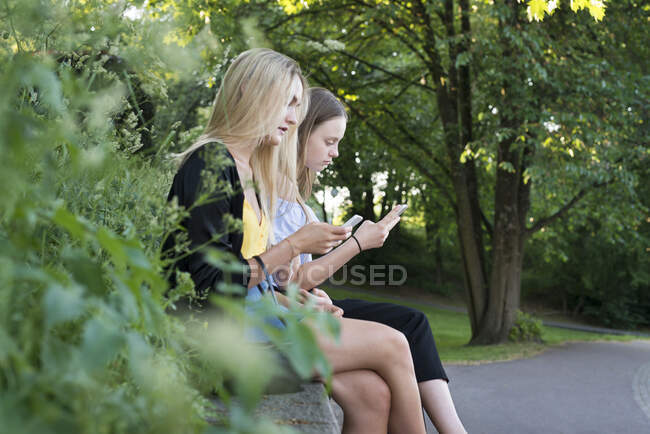 Sisters with smart phones sitting on bench — Stockfoto