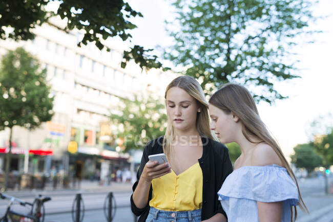 Sisters with smart phone in city — Stock Photo